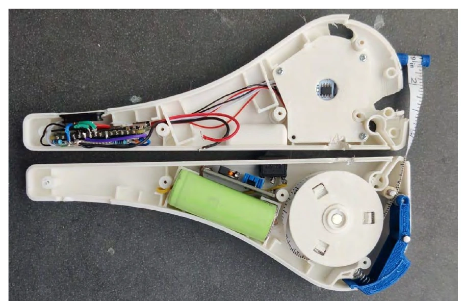 Open handheld prototype showing its battery, circuit boards, wiring and tape spool.