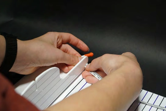Caregiver’s hands attaching the tape to the headrest’s measurement slot.